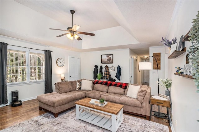 living area with wood finished floors, baseboards, a raised ceiling, and ceiling fan