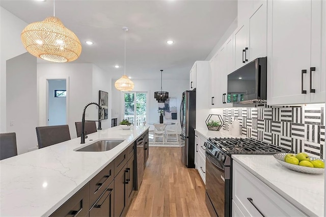 kitchen featuring tasteful backsplash, white cabinets, light wood-style flooring, stainless steel appliances, and a sink