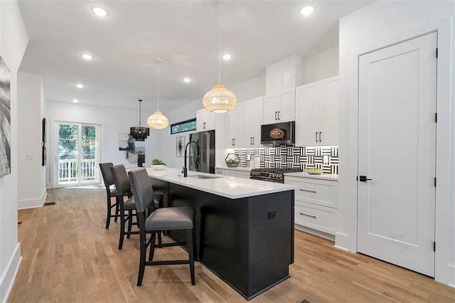 kitchen with appliances with stainless steel finishes, light wood-style flooring, an island with sink, and a kitchen bar