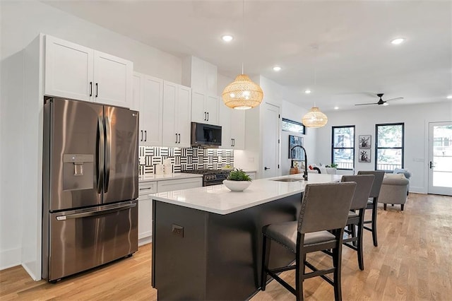 kitchen with a center island with sink, white cabinets, range with gas cooktop, stainless steel refrigerator with ice dispenser, and a sink