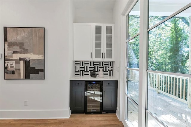 bar with beverage cooler, tasteful backsplash, baseboards, a bar, and light wood-type flooring