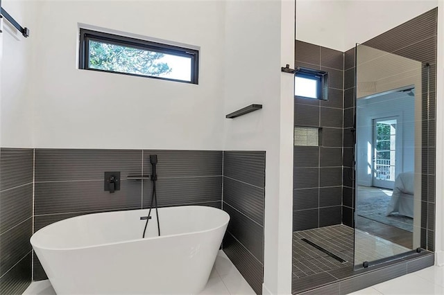 bathroom featuring a healthy amount of sunlight, a freestanding tub, and tile walls