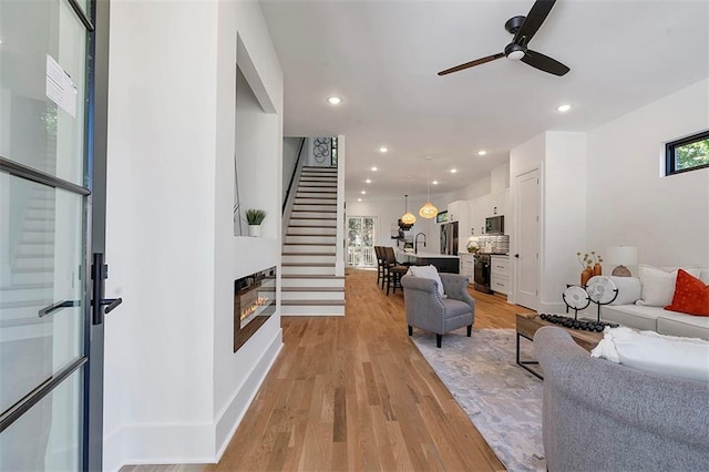 living room featuring baseboards, a glass covered fireplace, stairway, light wood-style floors, and recessed lighting