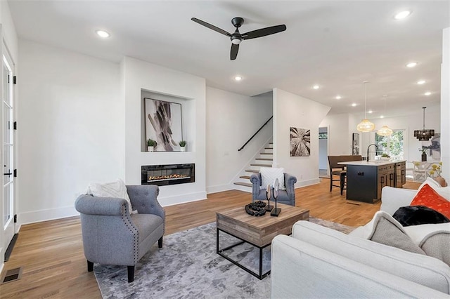 living area featuring light wood-type flooring, recessed lighting, stairway, and a glass covered fireplace