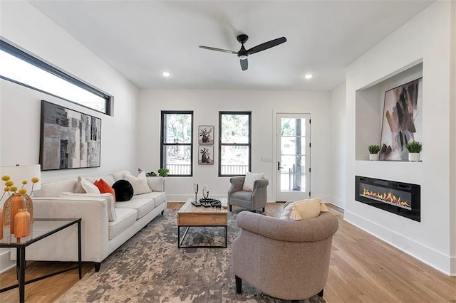 living room with recessed lighting, a ceiling fan, a glass covered fireplace, wood finished floors, and baseboards