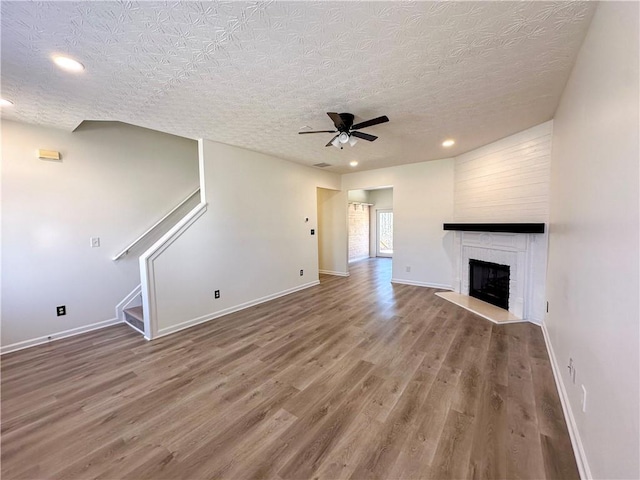 unfurnished living room with ceiling fan, a large fireplace, wood-type flooring, and a textured ceiling