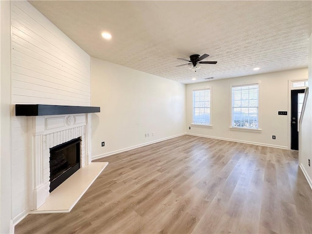 unfurnished living room with hardwood / wood-style flooring, ceiling fan, a fireplace, and a textured ceiling