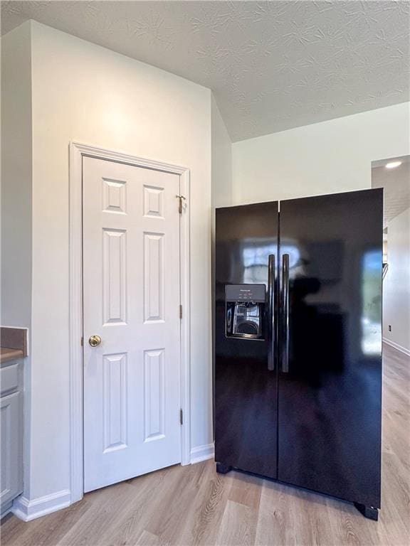 kitchen featuring a textured ceiling, black refrigerator with ice dispenser, and light hardwood / wood-style flooring