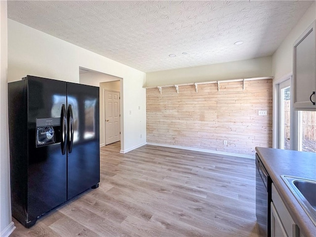 kitchen with dishwasher, black fridge with ice dispenser, light hardwood / wood-style flooring, and wood walls