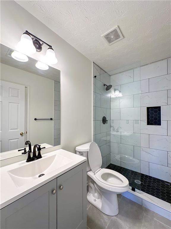 bathroom with vanity, tile patterned flooring, toilet, tiled shower, and a textured ceiling