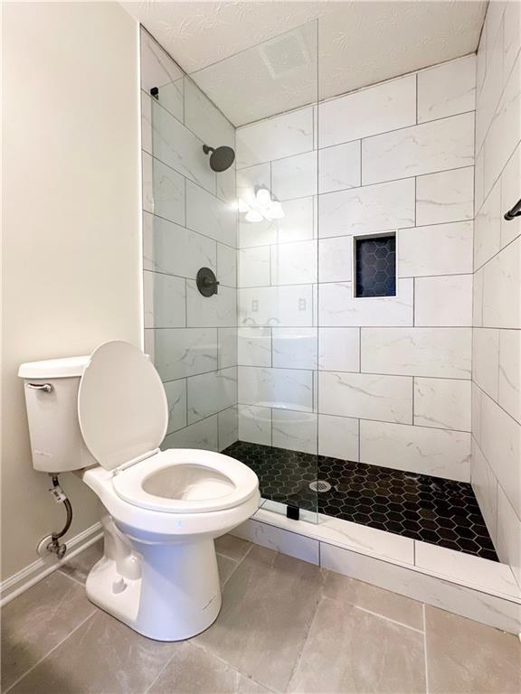 bathroom with tiled shower, tile patterned floors, and toilet