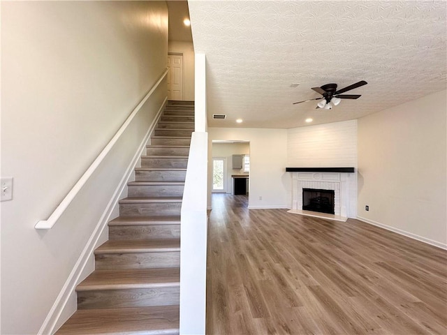 staircase with ceiling fan, a fireplace, wood-type flooring, and a textured ceiling