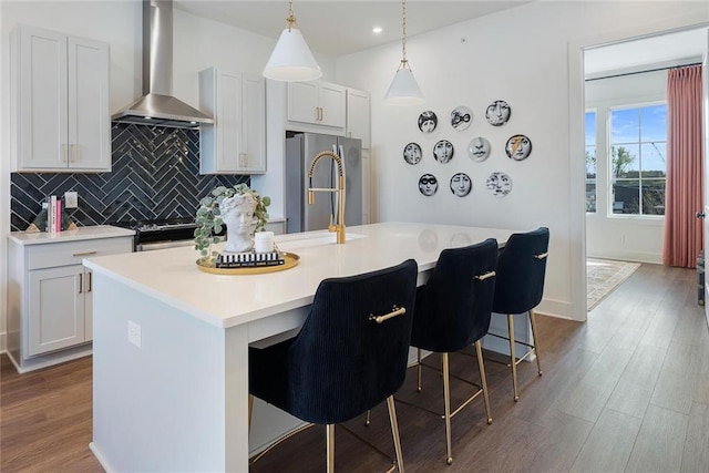 kitchen featuring wall chimney range hood, a kitchen breakfast bar, stainless steel appliances, a kitchen island with sink, and white cabinets