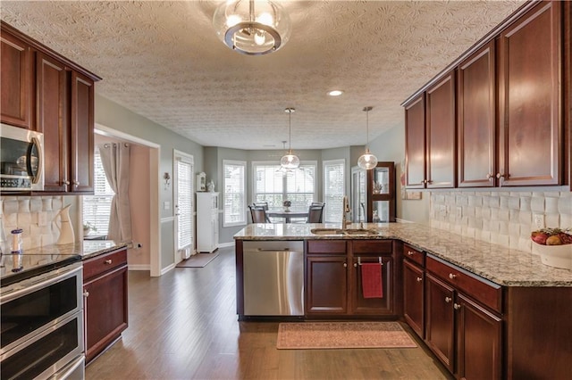 3370 Battlement Cir, Loganville, GA 30052 - kitchen featuring appliances with stainless steel finishes, a peninsula, dark wood-style floors, tasteful backsplash, and light stone countertops