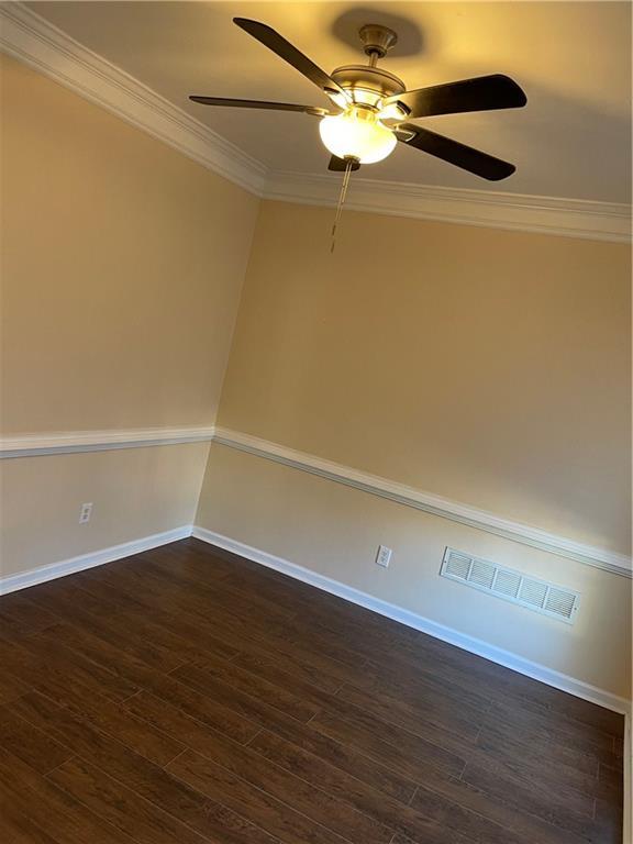 empty room featuring crown molding, dark wood-type flooring, and ceiling fan