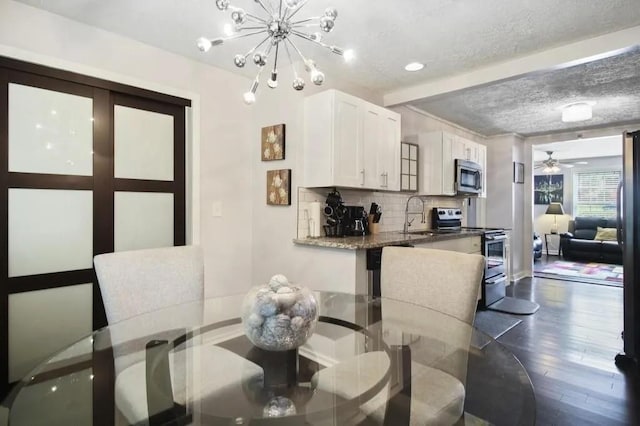 dining space featuring sink, dark hardwood / wood-style floors, ceiling fan with notable chandelier, and a textured ceiling