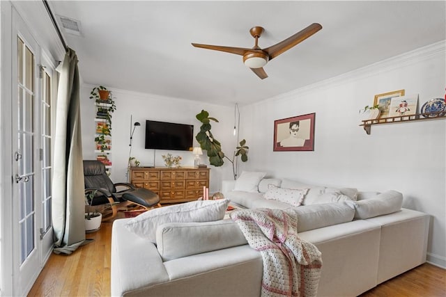 living room featuring crown molding, a ceiling fan, visible vents, and light wood finished floors