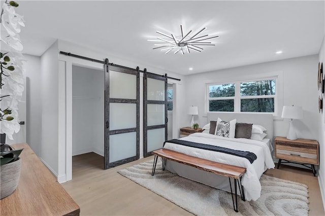 bedroom with light wood-type flooring, an inviting chandelier, recessed lighting, and a barn door