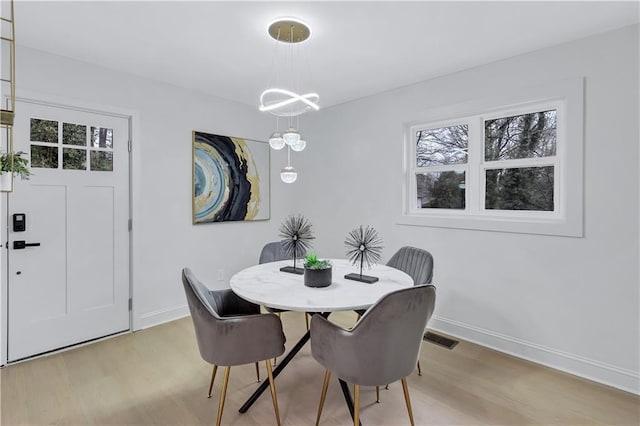 dining space featuring an inviting chandelier, light wood-type flooring, visible vents, and baseboards