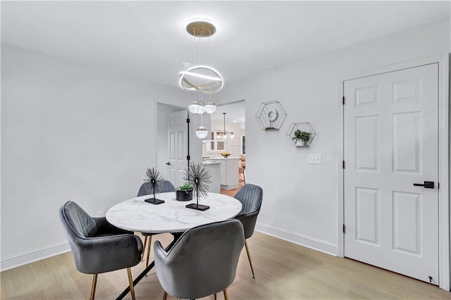 dining area with baseboards, light wood finished floors, and an inviting chandelier