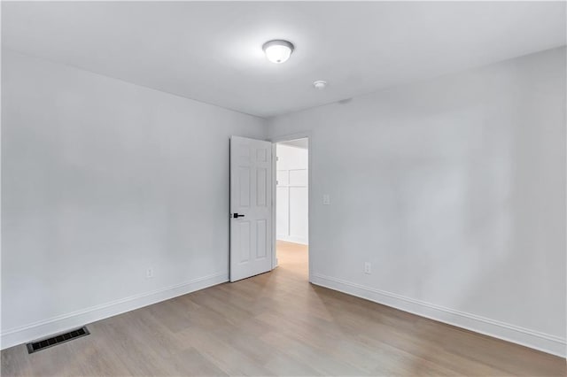 spare room featuring wood finished floors, visible vents, and baseboards