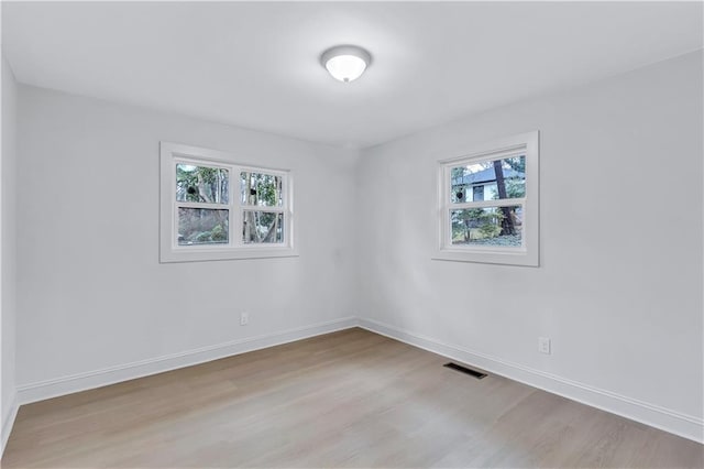 empty room with wood finished floors, visible vents, and baseboards