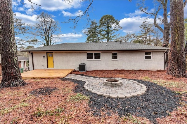 rear view of house with central air condition unit, a fire pit, a deck, and brick siding