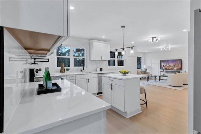 kitchen featuring light wood-style flooring, a sink, white cabinets, stainless steel dishwasher, and a center island