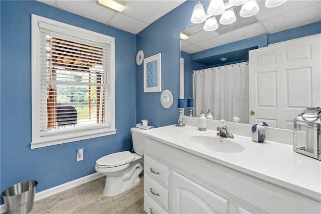 full bathroom featuring toilet, wood finished floors, baseboards, and a drop ceiling