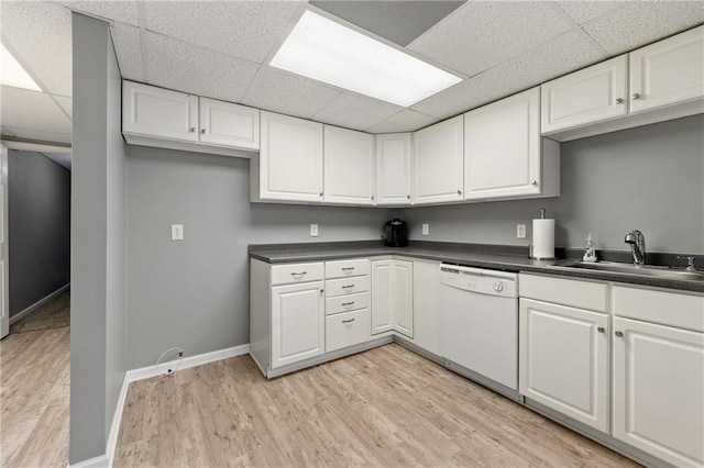 kitchen with a sink, dark countertops, white cabinets, white dishwasher, and light wood finished floors