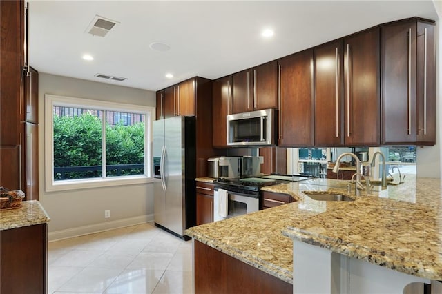 kitchen with light stone counters, a peninsula, a sink, visible vents, and appliances with stainless steel finishes