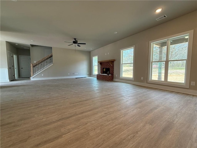 unfurnished living room with light wood-type flooring, ceiling fan, a fireplace, and visible vents