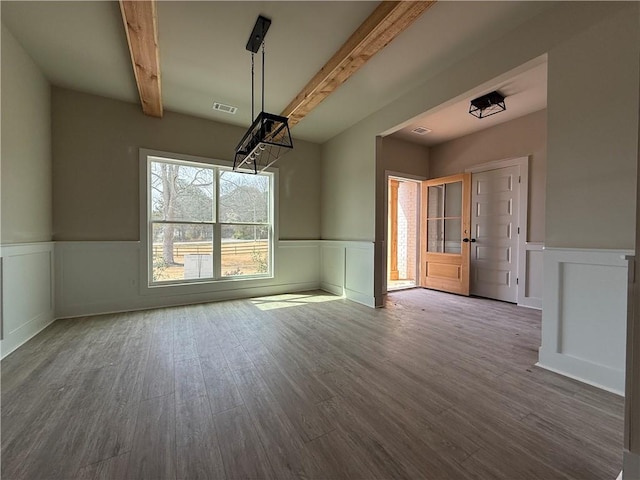 unfurnished dining area featuring a wainscoted wall, beamed ceiling, wood finished floors, and visible vents