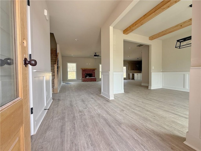 interior space with visible vents, ceiling fan, beamed ceiling, light wood-type flooring, and a brick fireplace