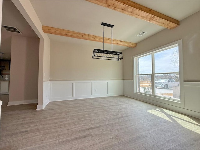 unfurnished dining area featuring light wood-style floors, wainscoting, visible vents, and beamed ceiling