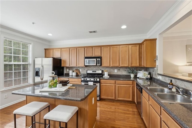 kitchen with appliances with stainless steel finishes, a breakfast bar, sink, crown molding, and light hardwood / wood-style flooring