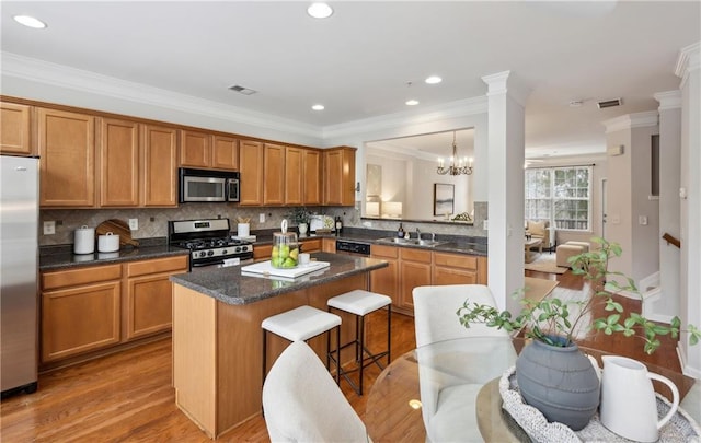 kitchen featuring a kitchen island, sink, hanging light fixtures, stainless steel appliances, and light wood-type flooring