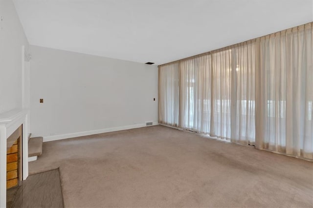 unfurnished living room with carpet flooring, a fireplace, visible vents, and baseboards