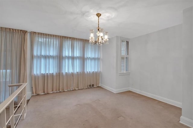 carpeted spare room featuring a notable chandelier and baseboards