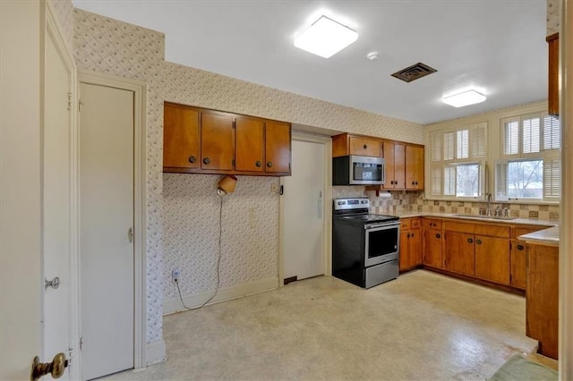 kitchen featuring visible vents, brown cabinets, a sink, appliances with stainless steel finishes, and wallpapered walls