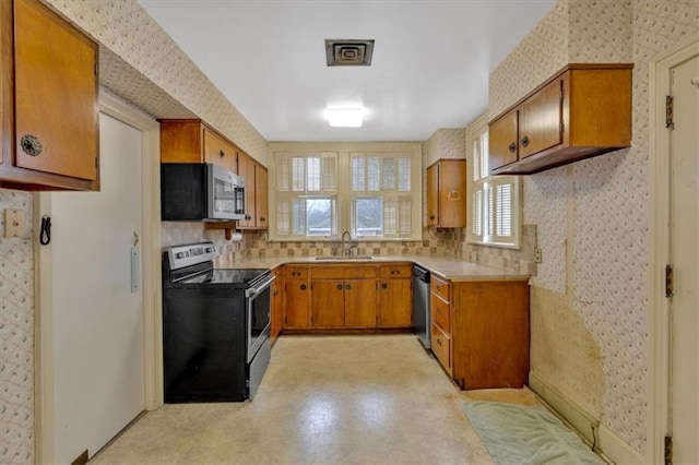 kitchen with wallpapered walls, a sink, brown cabinets, and stainless steel appliances