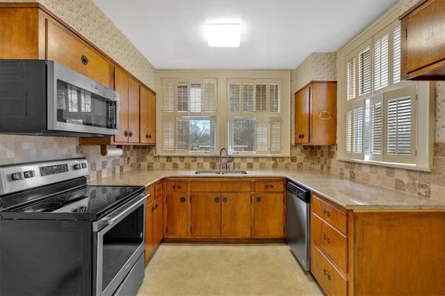 kitchen featuring wallpapered walls, brown cabinetry, appliances with stainless steel finishes, and a sink