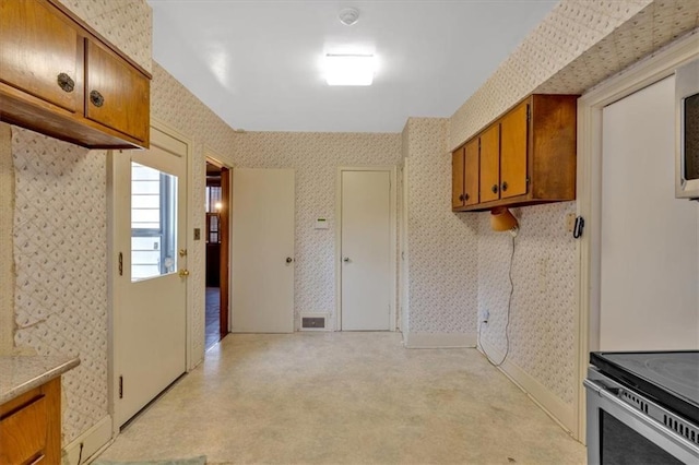 kitchen with baseboards, brown cabinets, light countertops, and wallpapered walls