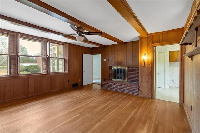 unfurnished living room featuring ceiling fan, wood walls, light wood-type flooring, beam ceiling, and a fireplace