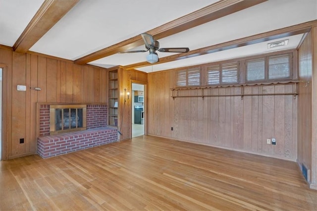 unfurnished living room featuring beam ceiling, a ceiling fan, wood finished floors, wood walls, and a brick fireplace