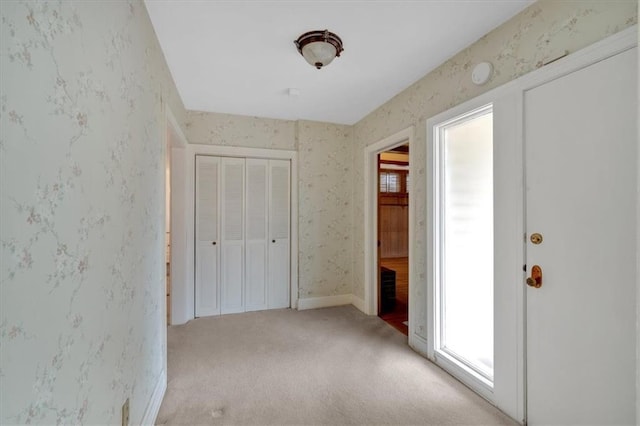 unfurnished bedroom featuring wallpapered walls, light colored carpet, a closet, and baseboards