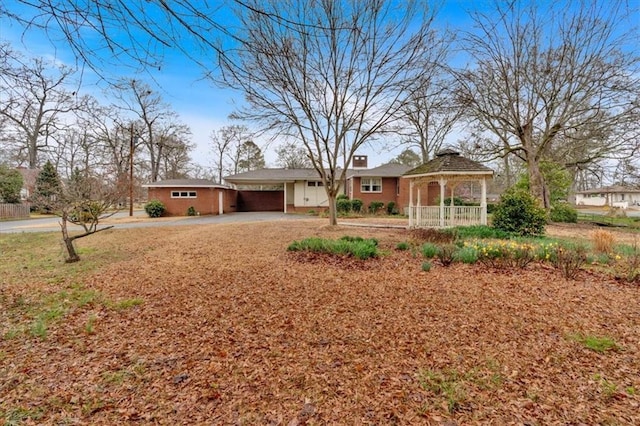 ranch-style home with a gazebo, an attached garage, a chimney, and driveway