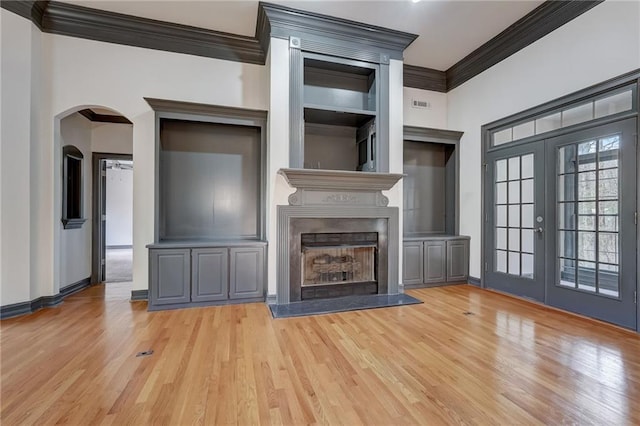 unfurnished living room featuring a high end fireplace, french doors, crown molding, and light hardwood / wood-style floors