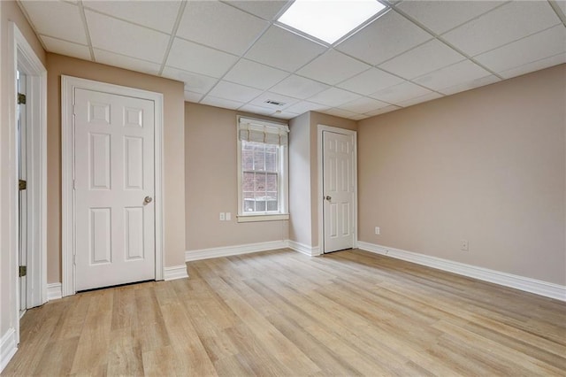 spare room featuring a paneled ceiling and light hardwood / wood-style flooring