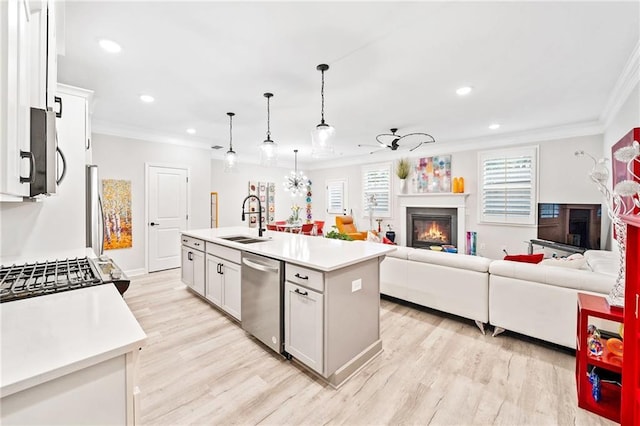 kitchen with appliances with stainless steel finishes, white cabinetry, sink, hanging light fixtures, and a center island with sink